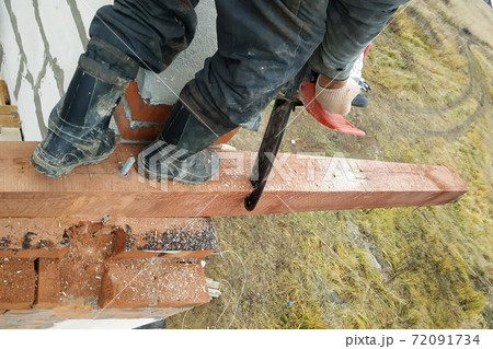 woodworker with a chainsaw makes drank on a wooden beam construction of houses woodworker with a chainsaw makes drank on a wooden beam construction of houses 72091734