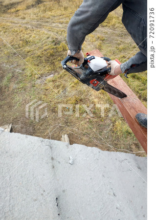 woodworker with a chainsaw makes drank on a wooden beam construction of houses 72091736