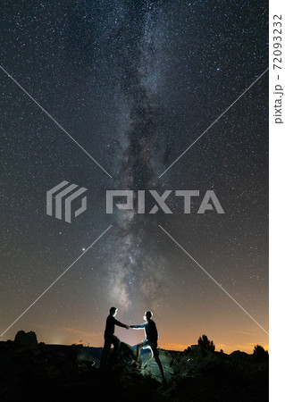 Two persons shaking hands against long milky way 72093232