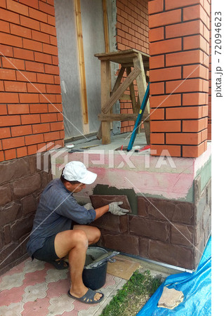 gluing a granite stone on the foundation of the building facing 72094623