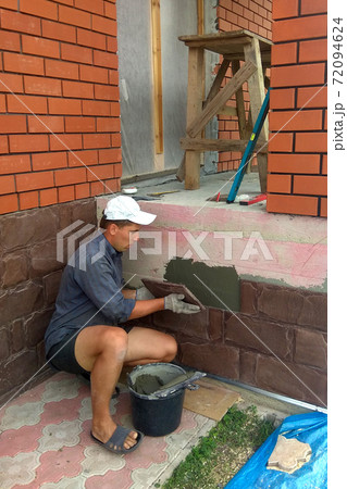 gluing a granite stone on the foundation of the building facing 72094624