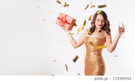 Young woman holding a gift box and drinks champagne, having fun with golden confetti Young woman holding a gift box and drinks champagne, having fun with golden confetti 72096992