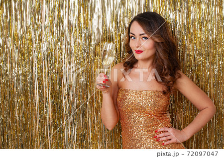 Portrait of a beautiful woman drinking champagne on a shiny gold background 72097047