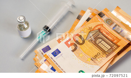 A stack of money lies near by a vaccine, medicine and syringe on a gray background 72097521