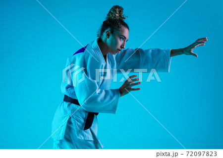 Professional female judoist training isolated on blue studio background in neon light. Healthy lifestyle, sport concept. 72097823