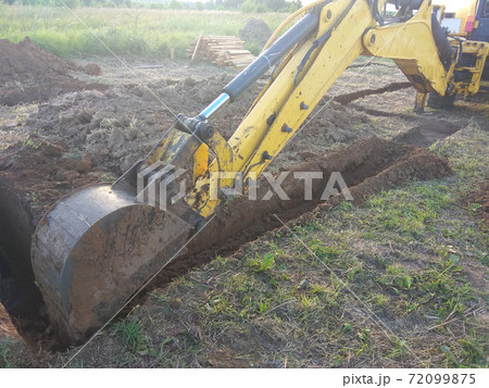 A work excavator digs a trench in a country house A work excavator digs a trench in a country house 72099875
