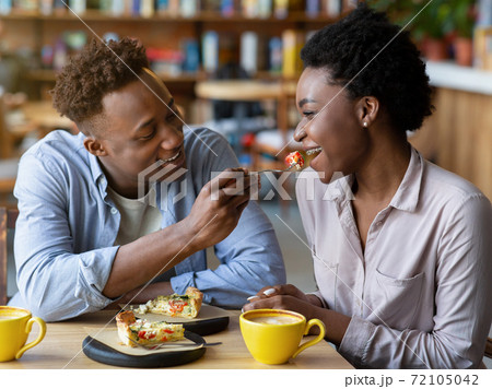 Millennial black guy feeding tasty quiche cake to his girlfriend at cozy urban cafe Millennial black guy feeding tasty quiche cake to his girlfriend at cozy urban cafe 72105042