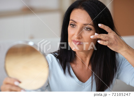 Adult woman checking her face in mirror, touching face 72105247