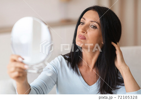 Adult woman checking her face in mirror 72105328