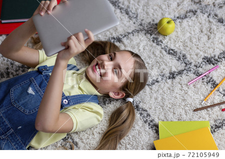 Girl lying on the floor carpet, holding and using tablet Girl lying on the floor carpet, holding and using tablet 72105949