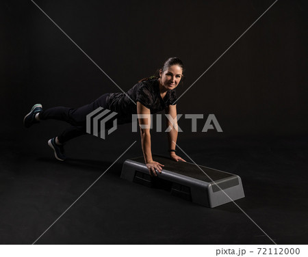 Fitness on the step platforms, in the bar pressed up the equipment keeps. Engaged in sports on a black background with a beautiful smile Fitness on the step platforms, in the bar pressed up the equipment keeps. Engaged in sports on a black background with a beautiful smile 72112000