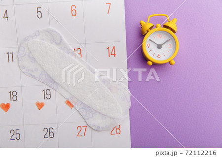 Calendar, menstrual pad and yellow alarm clock on lilac background. Female's menstrual cycle concept 72112216