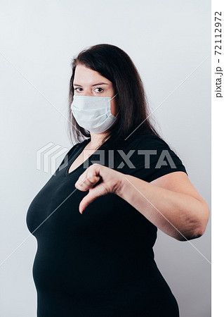 Woman in medical mask showing thumb down gesture 72112972