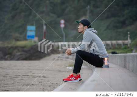 地方移住で、早朝に浜でゆっくりすごす男性 72117945