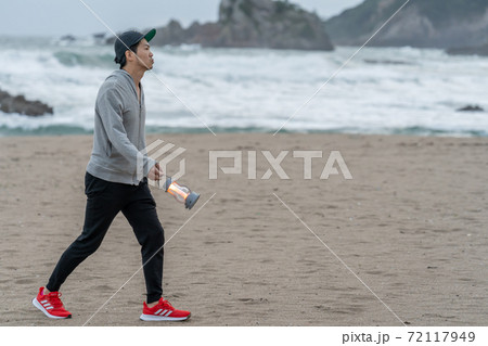 二地域暮らしで週末、早朝に浜を散歩してすごす男性 72117949