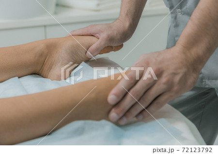 Male hands do massage of legs to patient girl. Young woman having massage in cosmetology clinic. Woman relaxing on massage table Male hands do massage of legs to patient girl. Young woman having massage in cosmetology clinic. Woman relaxing on massage table 72123792