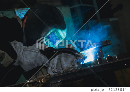 Close-up blacksmith welder in protective mask works with metal steel and iron using a welding machine, bright sparks and flashes. Welder uses a mask to protect your eyes from sparks. Close-up blacksmith welder in protective mask works with metal steel and iron using a welding machine, bright sparks and flashes. Welder uses a mask to protect your eyes from sparks. 72123814