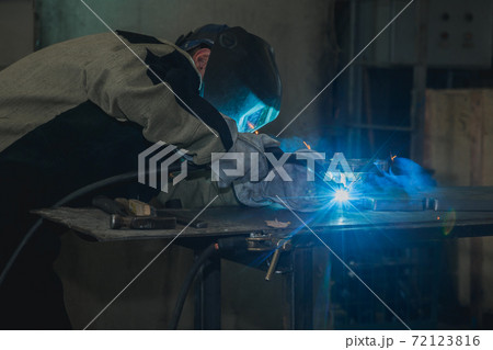 Industrial worker in protective mask using modern welding machine for welding metal construction on production manufacture at metalworking factory. 72123816