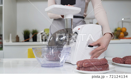 Making minced meat in electric meat grinder from fresh beef at home. Electric mincer machine with fresh chopped meat. Preparation of minced beef with electric grinder. Written on apron: best recipes 72124134