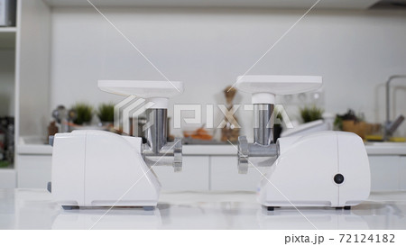 Two white electric meat grinders on white table in kitchen at home. Electric mincer machine for fresh chopped meat. Preparation of minced beef with an electric meat grinder. 72124182
