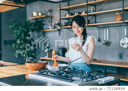 スマホを見ながら料理をする女性 72126934