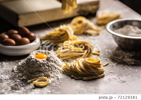 Nests of fresh fettuccine pasta with eggs, egg yolk, flour on a kitchen prep tabler on a kitchen prep table. Nests of fresh fettuccine pasta with eggs, egg yolk, flour on a kitchen prep tabler on a kitchen prep table. 72129381