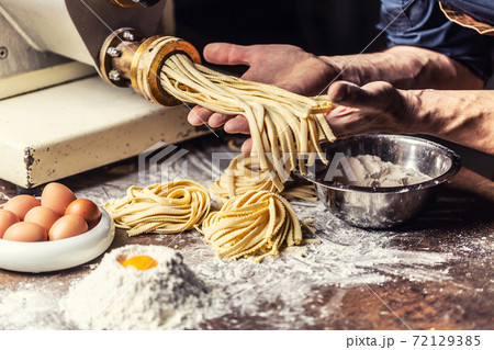 Fresh fettuccine egg dough pasta nests and hands of the chef holding another dose of the Italian specialty Fresh fettuccine egg dough pasta nests and hands of the chef holding another dose of the Italian specialty 72129385