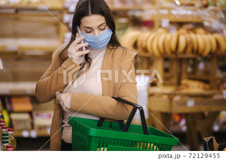 Buyer wearing a protective mask and gloves in supermarket. Shopping during the pandemic quarantine Covid-19. Nonperishable smart purchased household pantry groceries preparation. Woman spear by phone 72129455