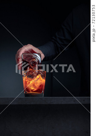 Alcoholic drink pouring from a bottle into a frosted glass with ice. 72130753