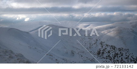 Snow covered winter mountains in last evening sunlight. Magnificent windy dusk on tops above picturesque alpine ski resort Snow covered winter mountains in last evening sunlight. Magnificent windy dusk on tops above picturesque alpine ski resort 72133142