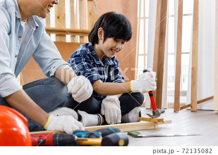 Asian boy sitting beside his father and using hammer to remove nail from timber. Concept family doing hobby together. 72135082