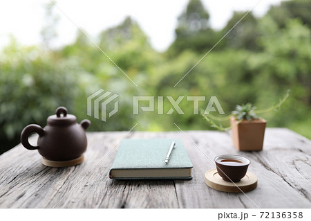 Brown traditional teapot and cup with green notebook on rustic grey wooden table 72136358