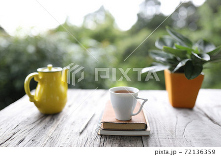 White teacup with leather book and yellow teapot with plant on wooden table 72136359