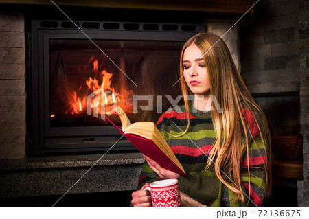 Girl reading by the fireplace sitting on the floor Girl reading by the fireplace sitting on the floor 72136675