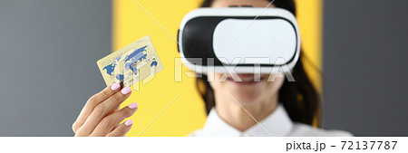 Woman is wearing virtual reality glasses in her hands she is holding bank credit card Woman is wearing virtual reality glasses in her hands she is holding bank credit card 72137787
