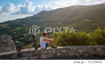 Young man riding an electric scooter on mountain range. Ecological transportation concept Young man riding an electric scooter on mountain range. Ecological transportation concept 72139042