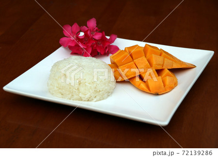 Thai mango sticky rice in the white square dish on the table, decorated with flowers. Thai mango sticky rice in the white square dish on the table, decorated with flowers. 72139286