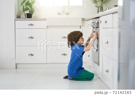 Restless little hispanic boy watching cake baking in the oven, crouching down in the kitchen 72142165