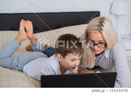 Blonde mom with glasses and teen son look at the laptop screen while lying on the couch. Education at home in quarantine. Lockdown Blonde mom with glasses and teen son look at the laptop screen while lying on the couch. Education at home in quarantine. Lockdown 72143470