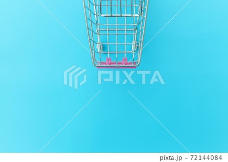 Small supermarket grocery push cart for shopping toy with wheels isolated on blue pastel colorful trendy background Copy space. Sale buy mall market shop consumer concept. 72144084