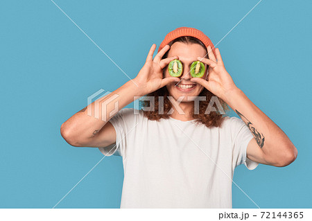 Young adult guy covered eyes with kiwi fruit Young adult guy covered eyes with kiwi fruit 72144365
