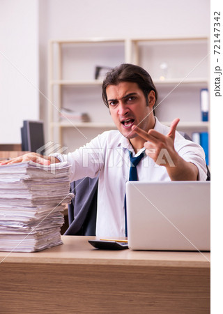 Young male employee unhappy with excessive work in the office 72147342