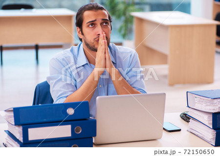 Young male employee and too much work in the office Young male employee and too much work in the office 72150650