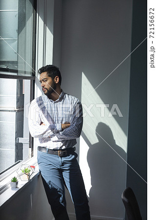 Mixed race man looking through a window in an office 72156672