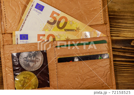 Wallet with fifty euro bills and bitcoins on wooden background Wallet with fifty euro bills and bitcoins on wooden background 72158525