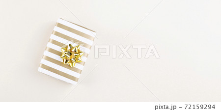 Gift in striped paper with golden bow on beige background. Top view. Copy space 72159294