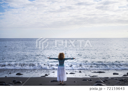 travel and freedom people lifestyle - Standing woman in back view with open arms for success or satisfaction concept image - blue sky and ocean view in background in front of her 72159643