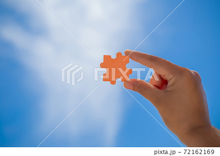 Woman holding an orange puzzle, Jigsaw alone wooden puzzle against over sky background. Woman holding an orange puzzle, Jigsaw alone wooden puzzle against over sky background. 72162169