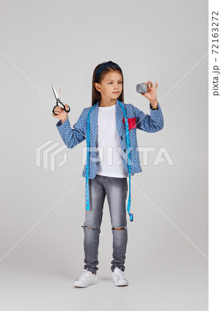 adorable little girl holding tape measure and spool of thread 72163272