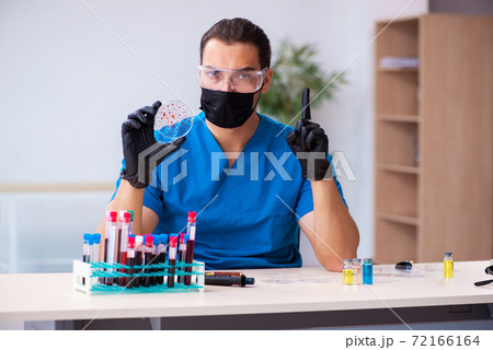 Young male biochemist testing blood samples in pandemic concept 72166164
